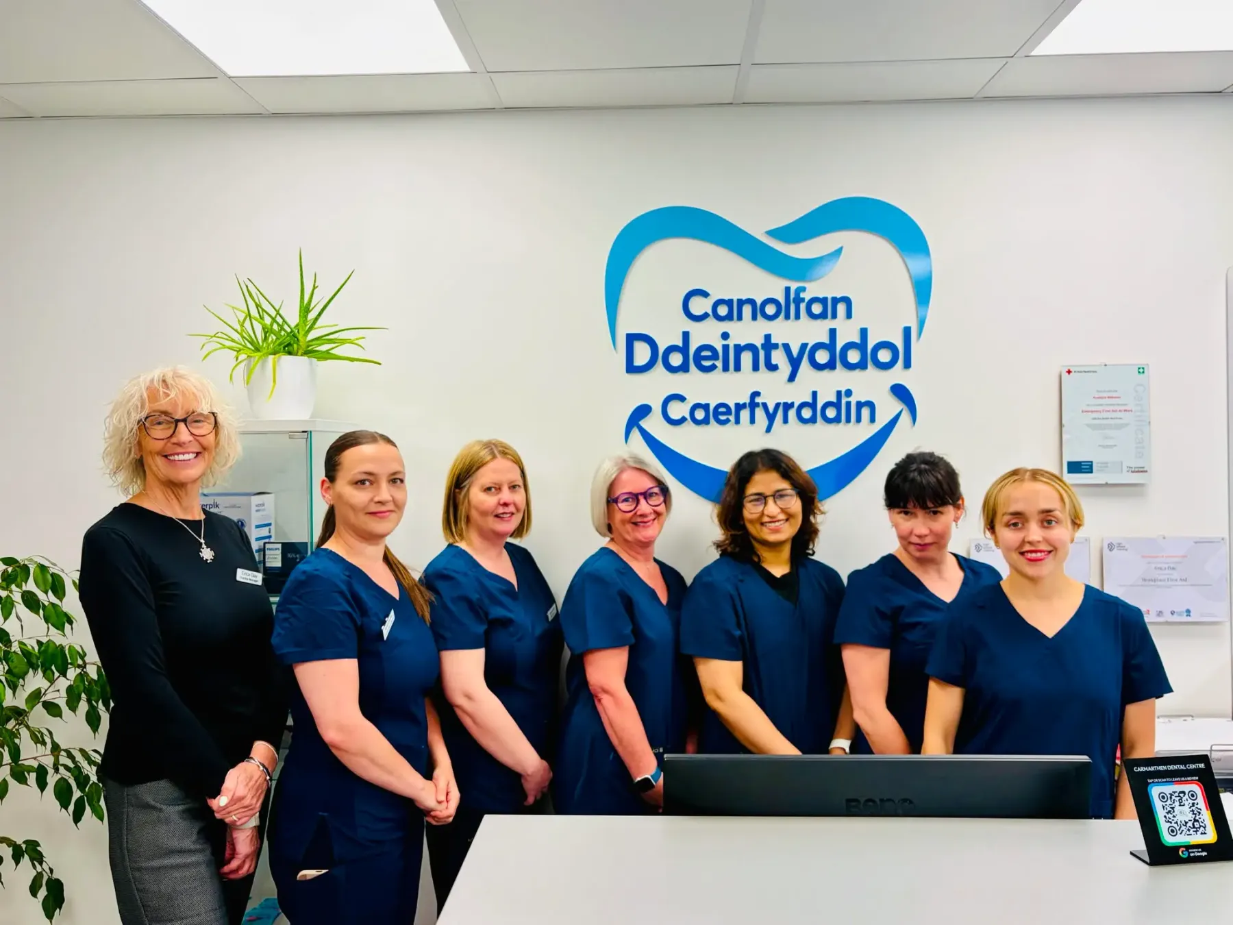 The Carmarthen Dental Centre team in navy scrubs, standing in front of the practice sign
